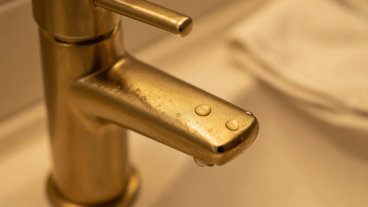 Macro view of textured gold faucet under warm vanity lighting.